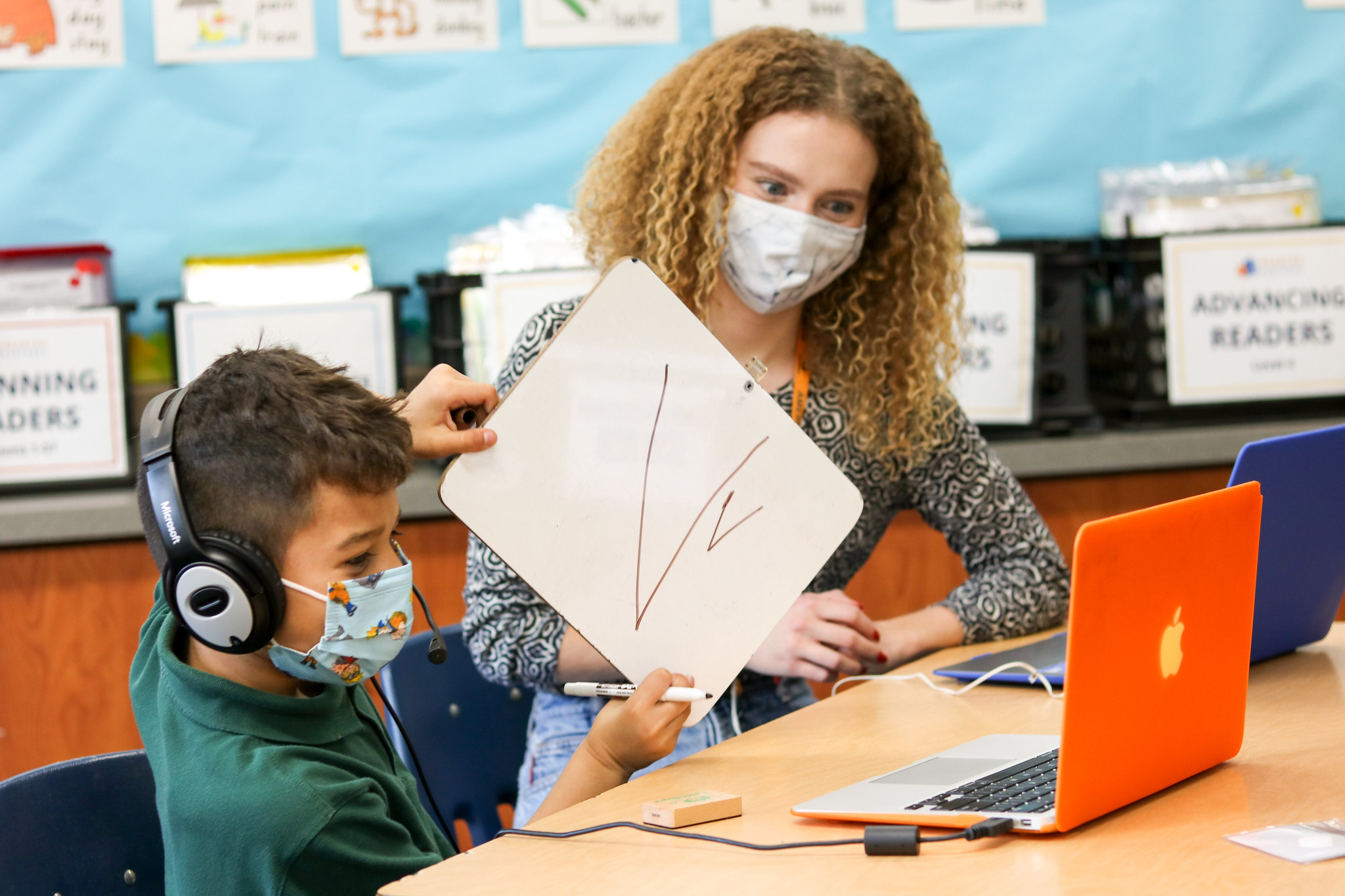 Student learning to read, holding up a whiteboard with the letter V on it, using his brain to identify a letter