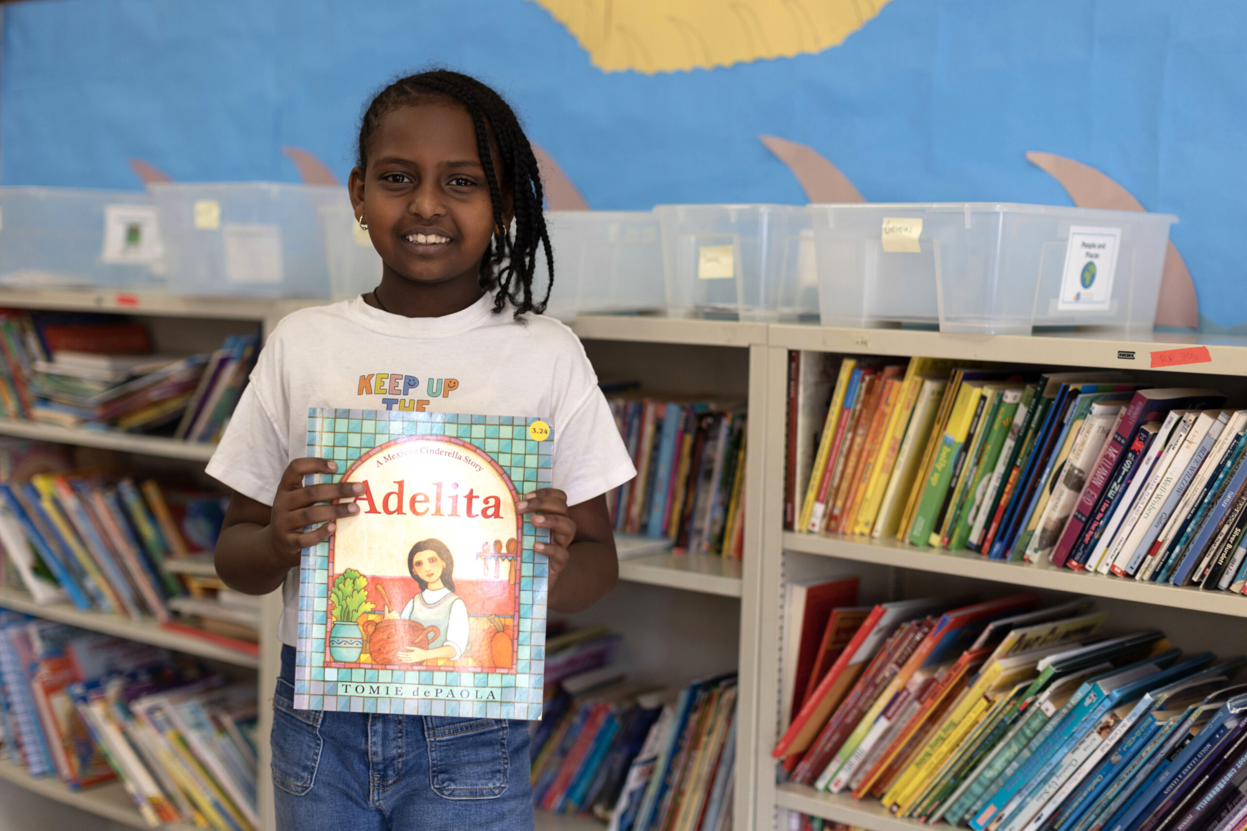 student holding up book "Adelita" in front of bookshelves