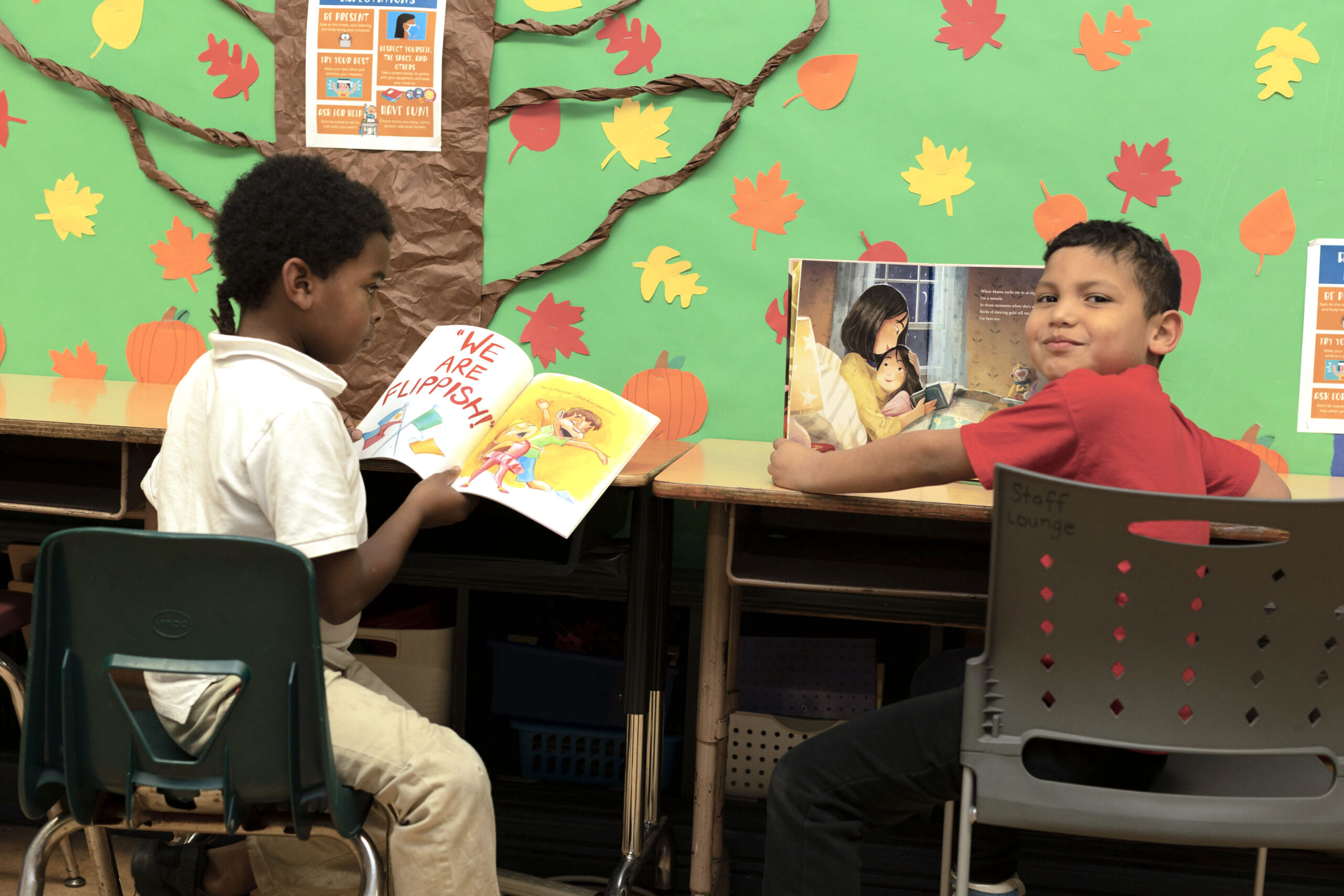 students reading at a desk, one student smiles at the camera