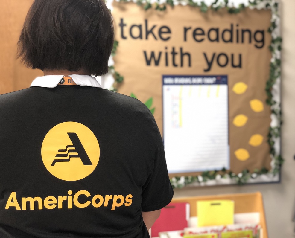 person standing in a classroom with their back to the camera,the AmeriCorps logo visible on the back of their shirt