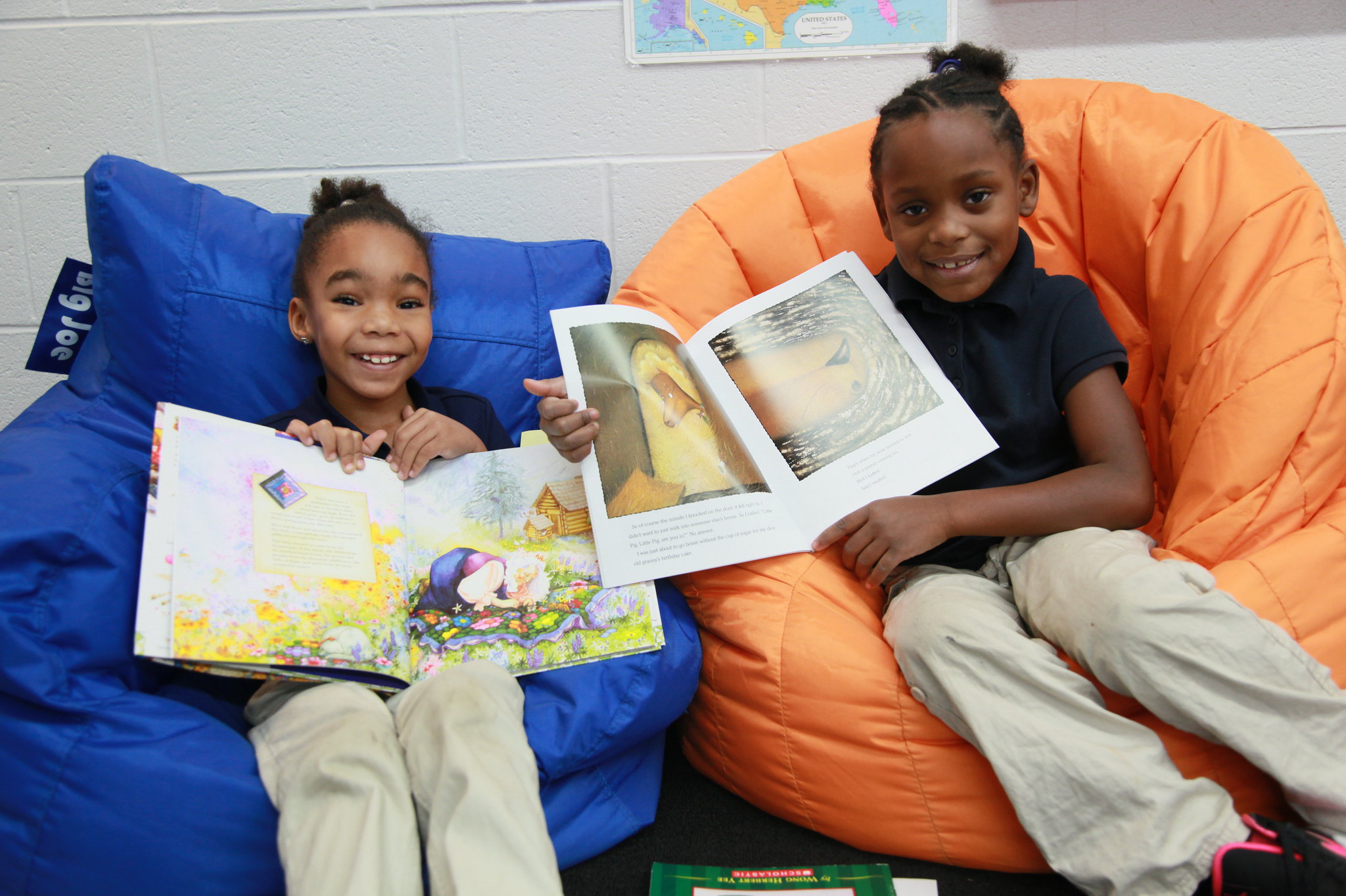 two female students sitting in bean bag chairs hold up the picture books they are reading, high-quality pre-k