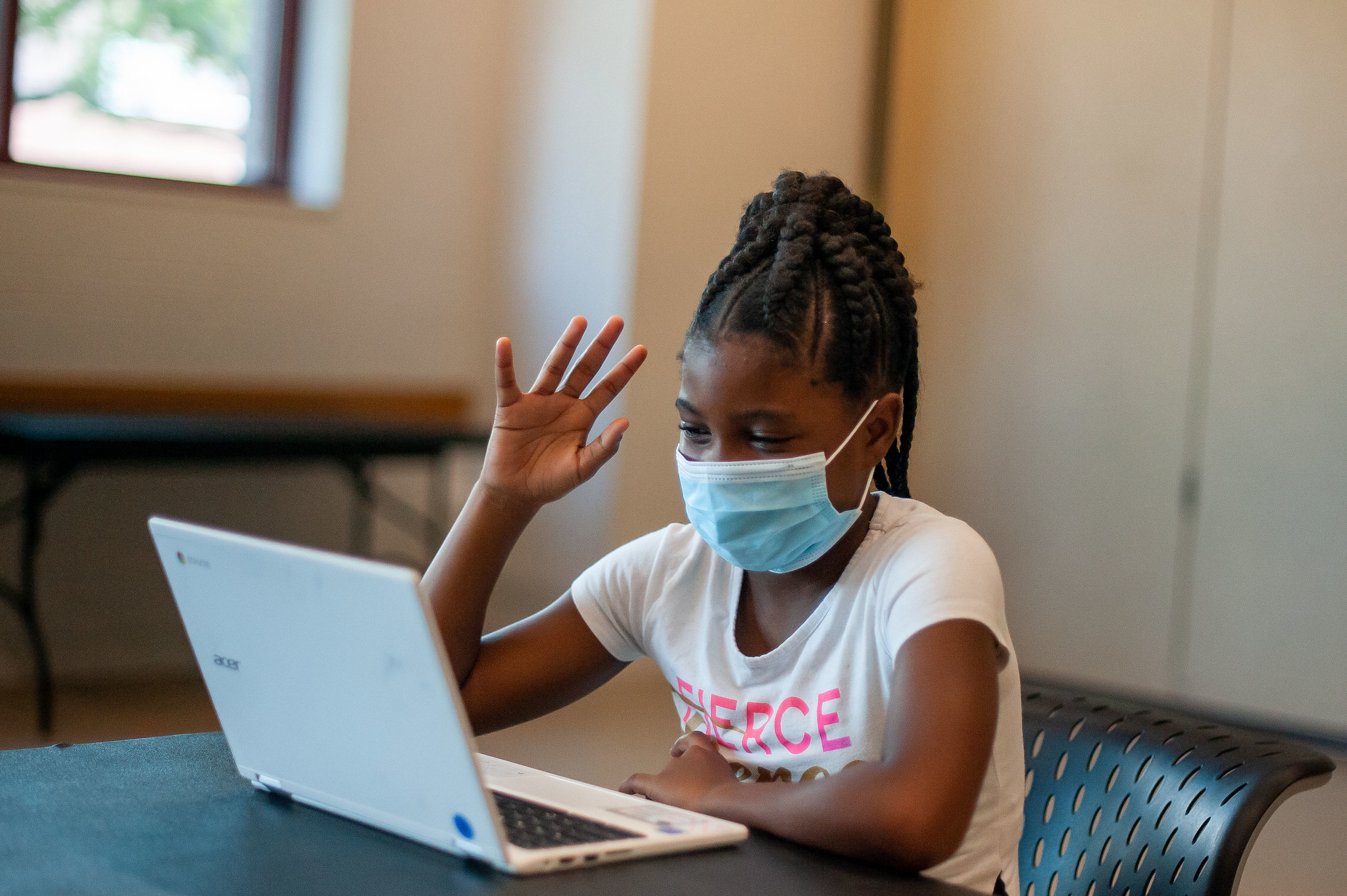 a reading partners student wearing a mask and waving at her computer, systematic phonics instruction