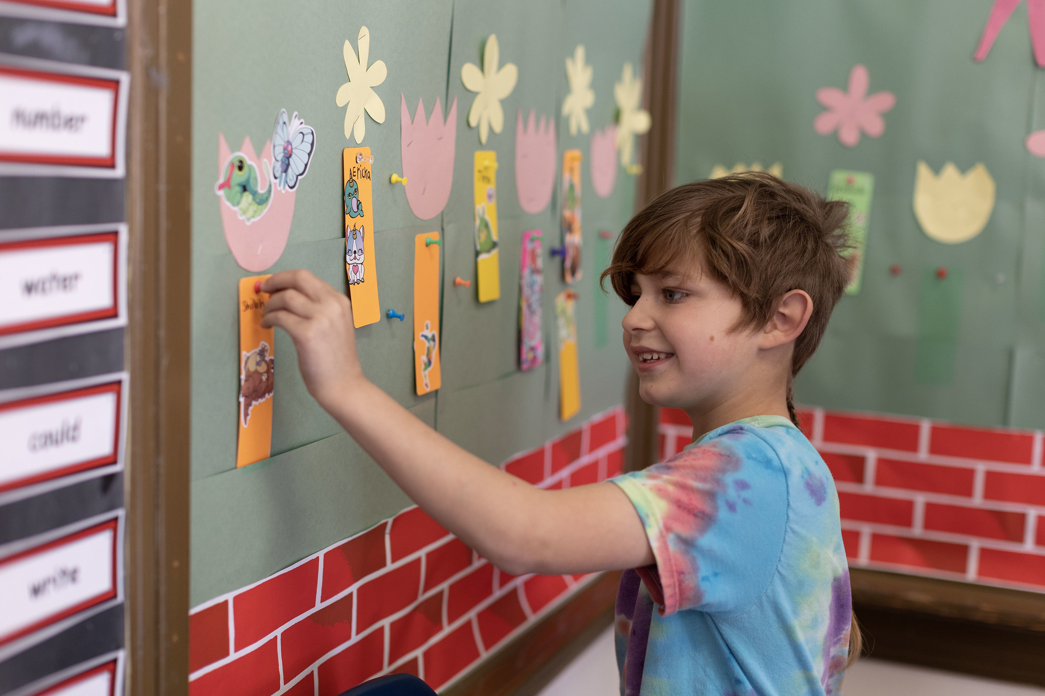 a young male student puts a sticker on his bookmark attached to a bulletin board