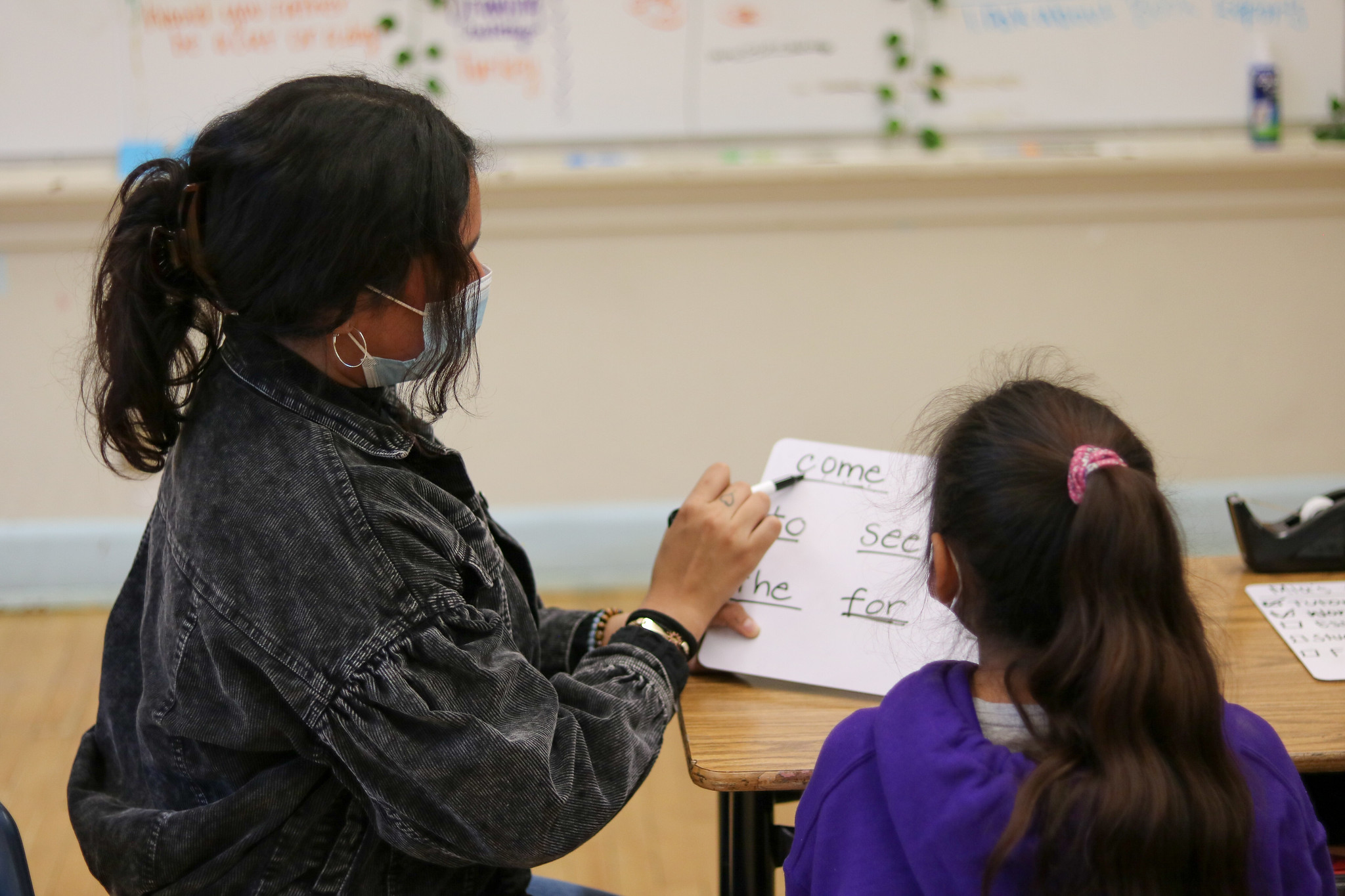 a tutor and student look at a whiteboard, where the word "come" is written