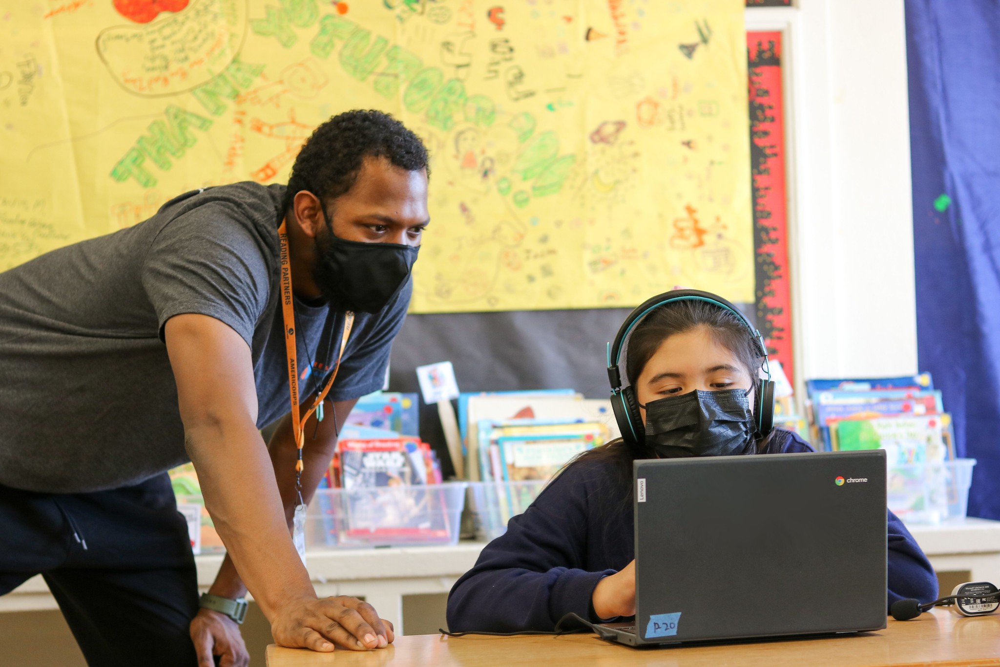 an americorps member leaning over a student's computer, assissting them with their literacy lesson