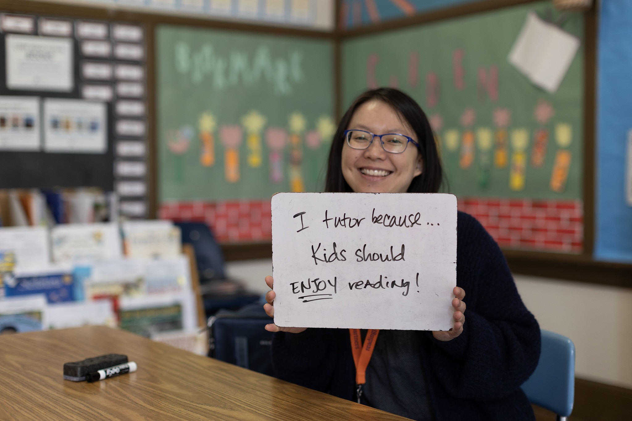 volunteering isn't just important, it's essential; tutor holding up a sign that says "I tutor because kids should enjoy reading!"