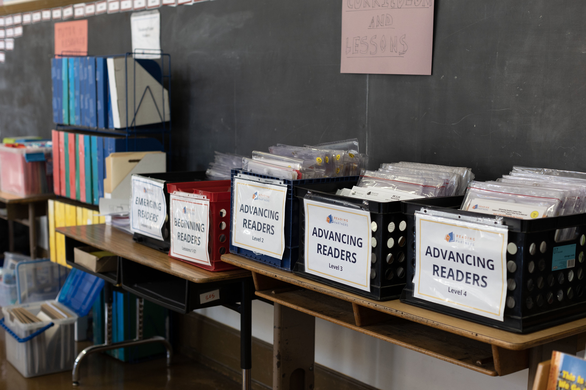 crates that hold our curriculum materials line a table in a reading center; science of reading and balanced literacy