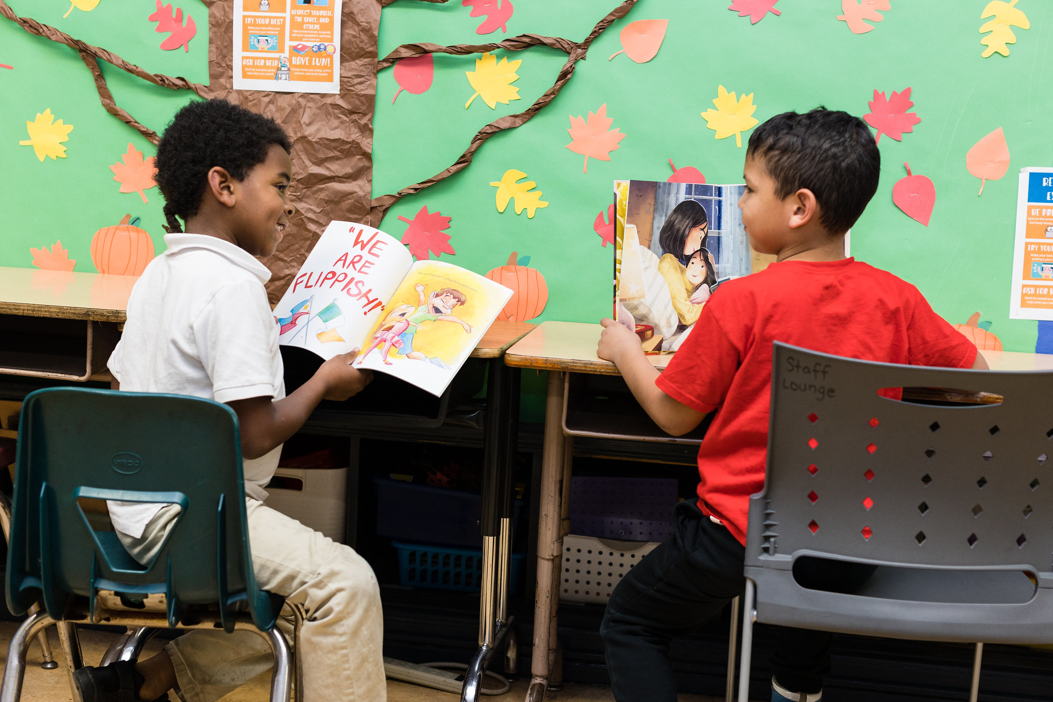 two students read their respective books at a table, they smile at each other; science of reading and balanced literacy