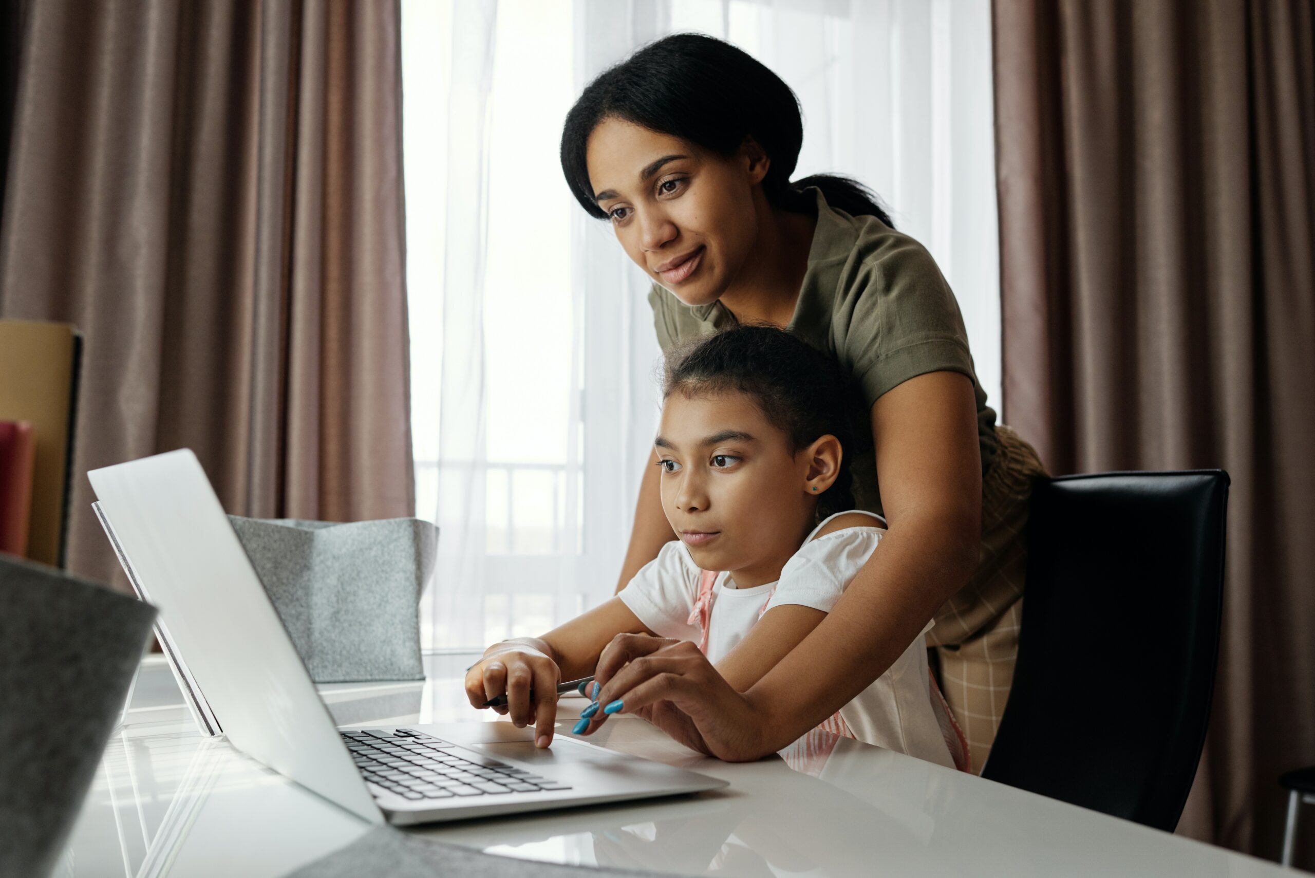 a mother helps her daughter on a computer 