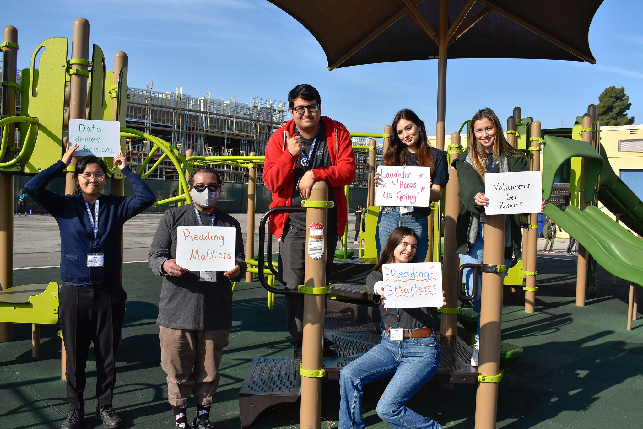 a group of americorps members stand at a playground holding signs that say our reading partners values, americorps gap year