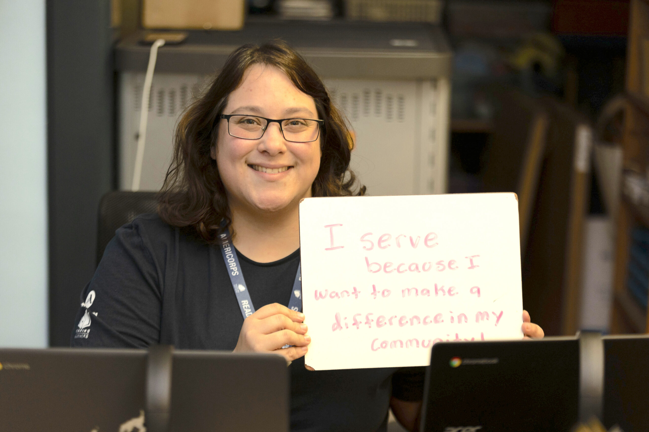 reading partners is ramping up innovation; an americorps member holds up a sign that says "I serve because I want to make a difference in my community"