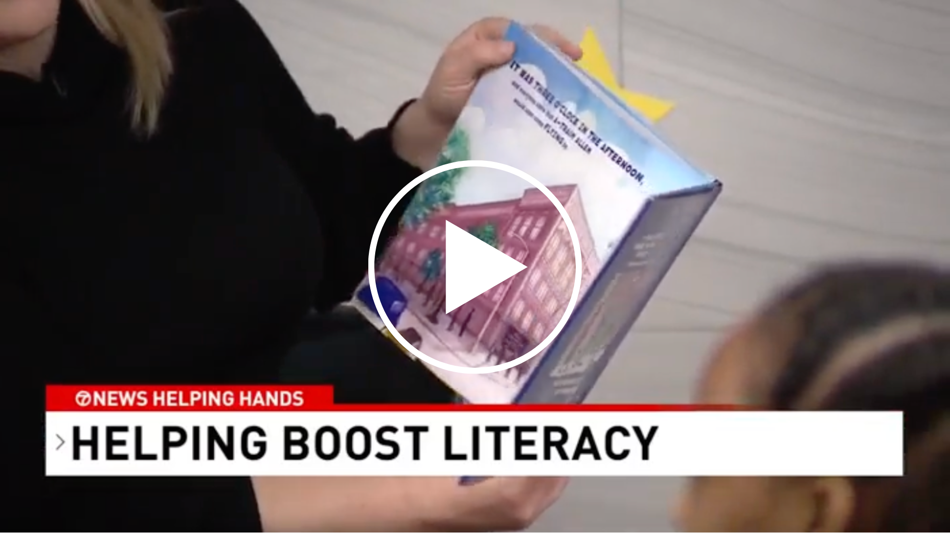 screenshot from a video showing a book held by a tutor and the banner at the bottom reads: helping boost literacy; Helping Hands, Easterns Automotive surprise Reading Partners