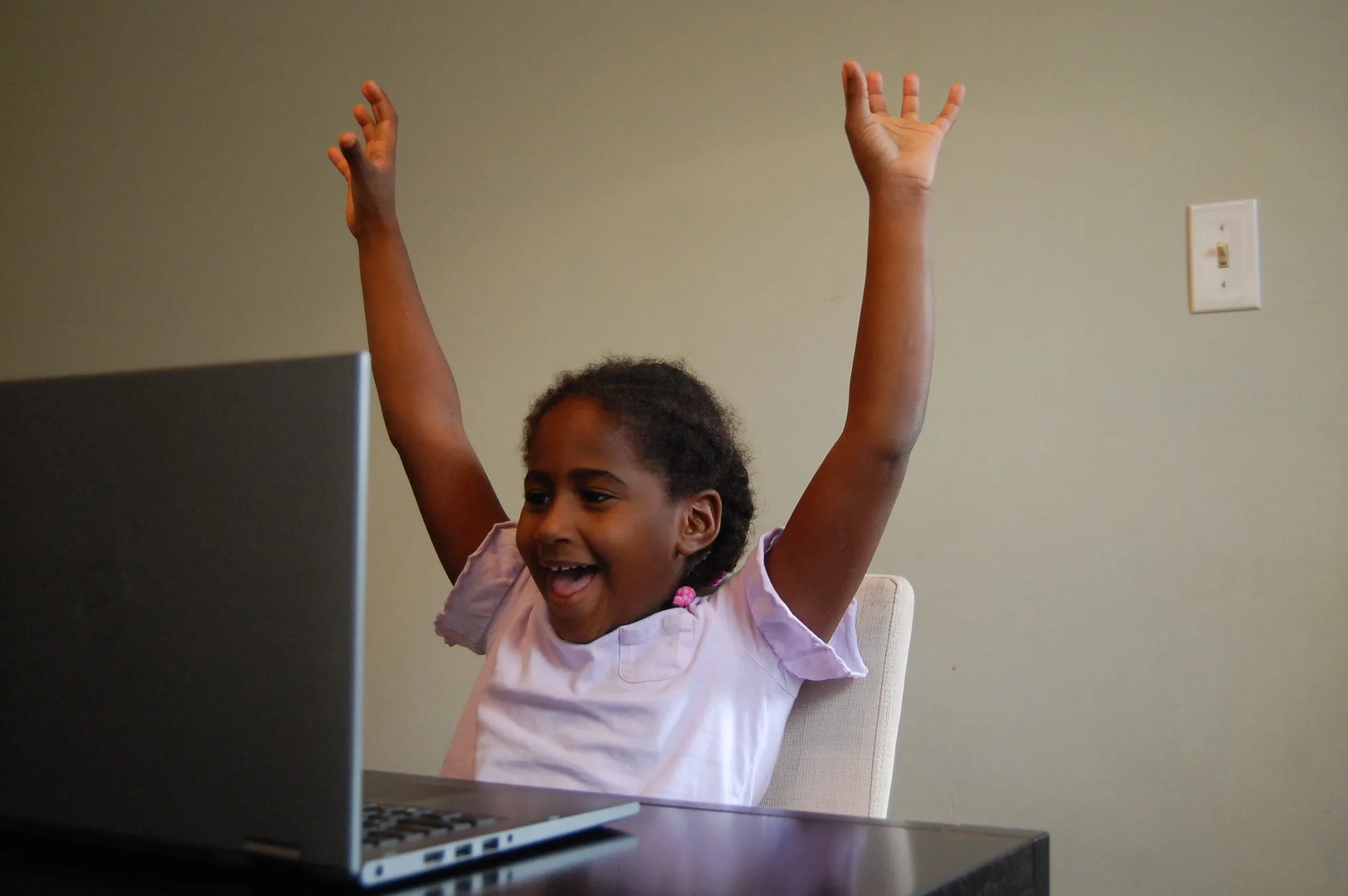 a student raising her hands while looking at a computer