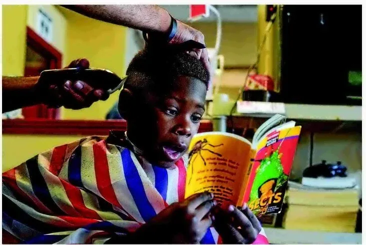 student getting a haircut and reading a book at the same time